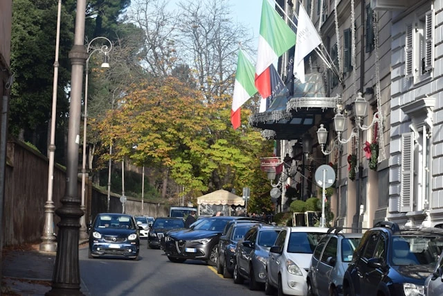Street view of a building lined with Italian flags and parked cars, representing the Consulate General of Italy in Kolkata