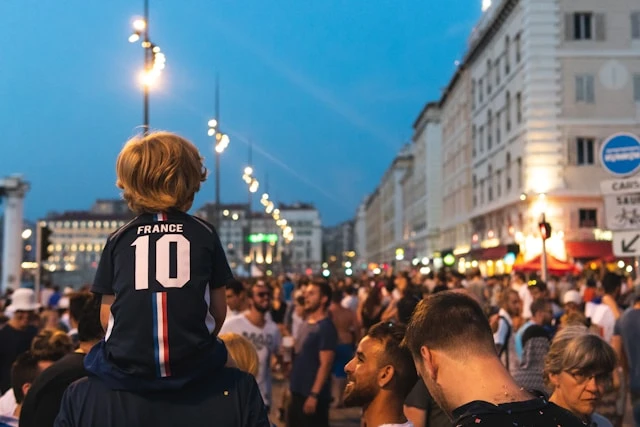 Crowd celebrating with a child wearing a France jersey, symbolizing French culture and travel, representing the experience of applying for a French visa through the France Consulate General in Houston.